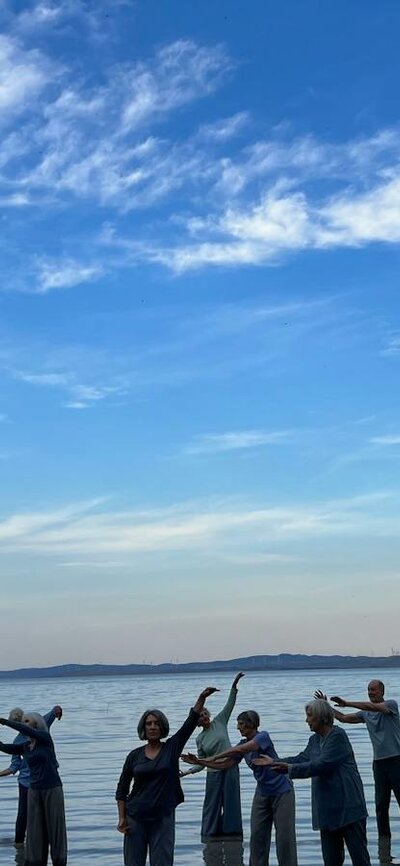 14 people standing knee deep in an expanse of water with a bright blue sky and fluffy white clouds