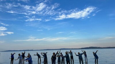 14 people standing knee deep in an expanse of water with a bright blue sky and fluffy white clouds