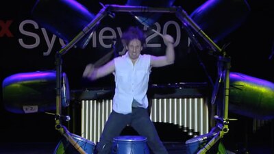 A man in a white shirt playing the drums.