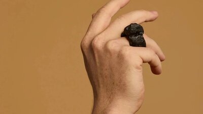 A hand wears a large ring carved out of a dark material against a tan background