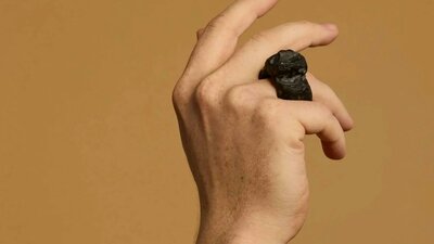 Matthew Freeman | Soma Erratics 1, 2025 A hand wears a large ring carved out of a dark material against a tan background