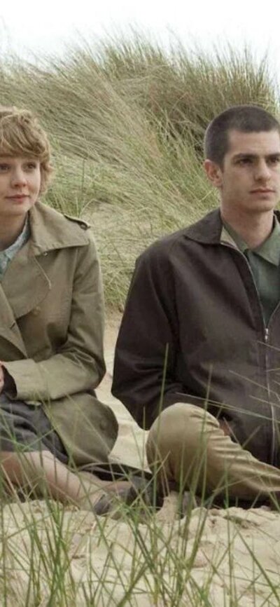 One woman and one man sitting rugged up in coats on a beach