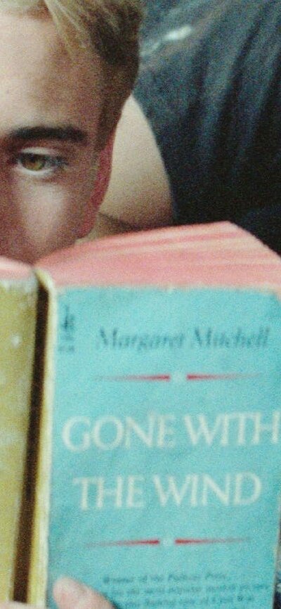 One male lying on couch sleeping, another sitting in front reading a book
