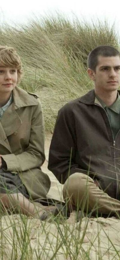 One woman and one man sitting rugged up in coats on a beach
