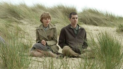 One woman and one man sitting rugged up in coats on a beach