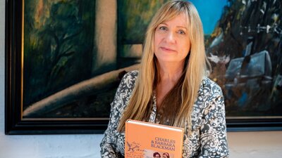 A portrait of a woman holding her written book 'Charles and Barbara Blackman.'