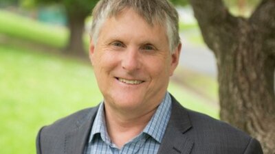 A photograph of a man with a tree and grass behind him.