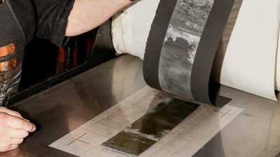 A photograph of hands peeling a print off of a press