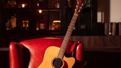 Acoustic guitar leaning on a red leather chair