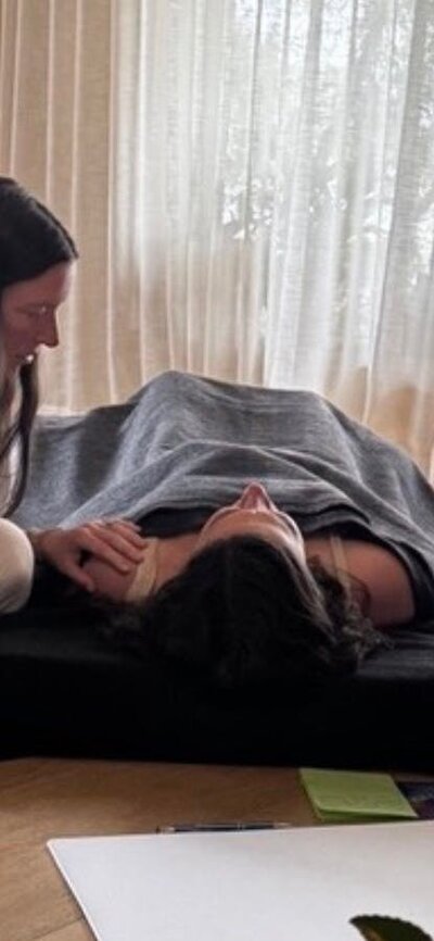 Facilitator (Shelby) sitting beside a participant lying comfortably on a mat during a session