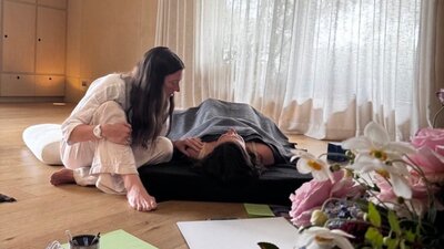 Facilitator (Shelby) sitting beside a participant lying comfortably on a mat during a session