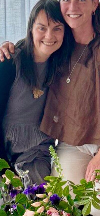 Two facilitators smiling together during a breathwork session with seasonal flowers in foreground