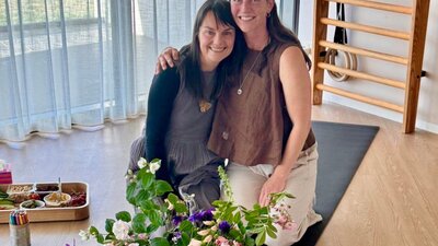 Two facilitators smiling together during a breathwork session with seasonal flowers in foreground