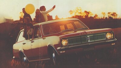 A Holden Kingswood car parked  on a grassy field at sunset with children hanging out of the windows