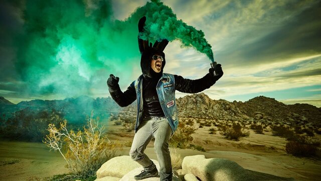 Bunny Racket A man dressed as a rabbit in the desert. Green smoke is coming from a can in his hand.