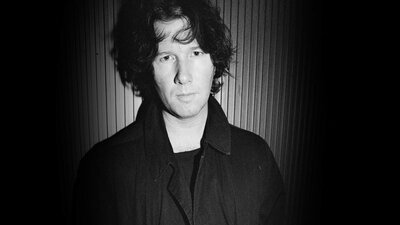 Black and white photo of Marc Dwyer standing in front of a striped wall.lle