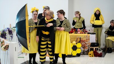 A group of dancers dressed in yellow and black reminiscent of bees perform with umbrella