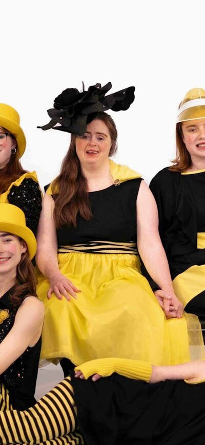 A group of dancers dressed in yellow and black reminiscent of bees pose for a group photograph