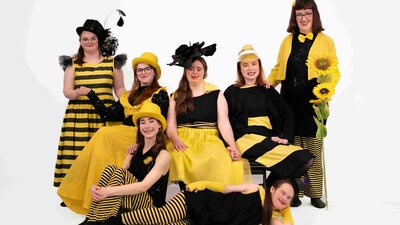 A group of dancers dressed in yellow and black reminiscent of bees pose for a group photograph