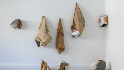 Series of hessian sacks, packaging cardboards, plaster and other materials on a wall.