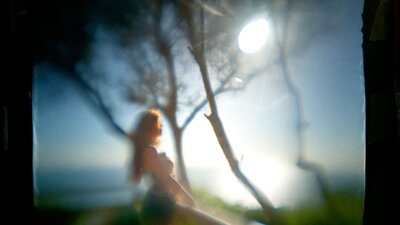 A photograph of a woman standing at a lookout overlooking the beach, surrounded by trees