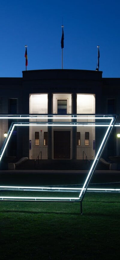 Neon light sculpture on the grass of the National Film and Sound Archive. Photo taken at night.