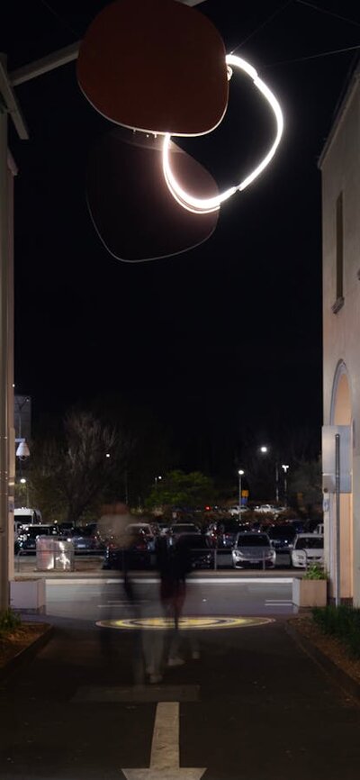 A neon sculpture hanging in an alley way at night.
