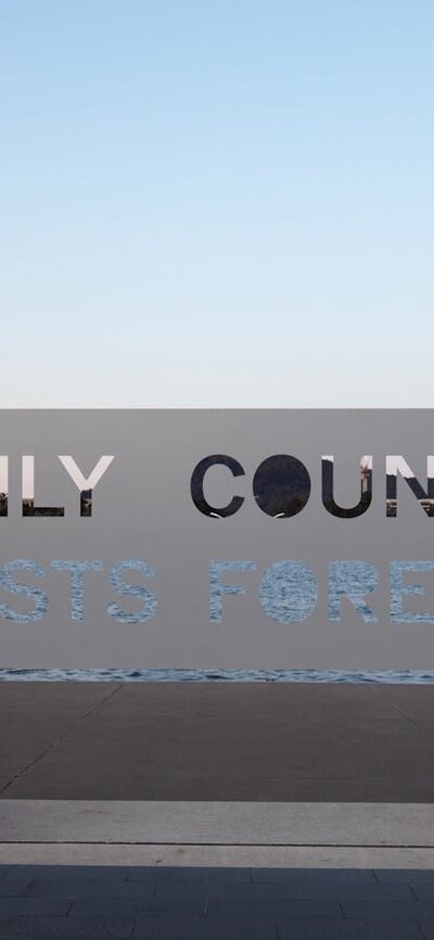 A metal sign that reads "Only Country Lasts Forever" positioned in front of Lake Burley Griffin.