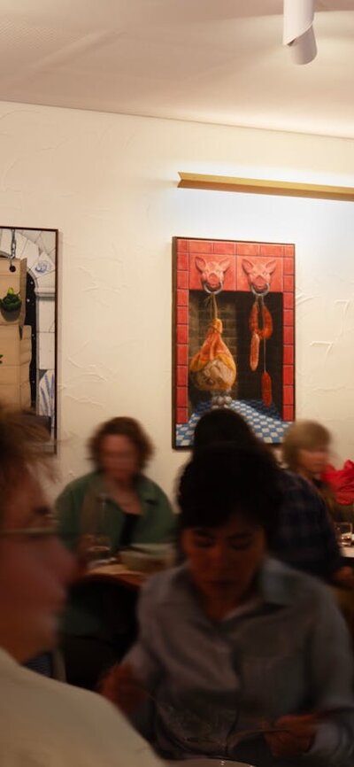 A restaurant full of people moving, with colourful paintings hung on the walls.
