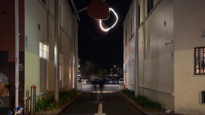 A neon sculpture hanging in an alley way at night.