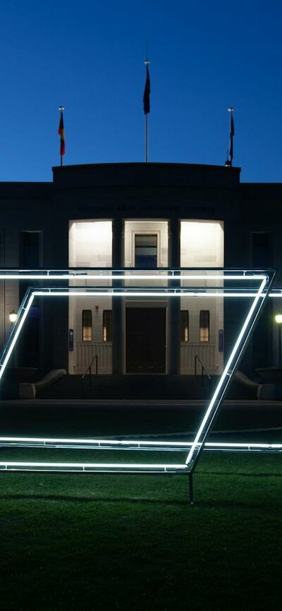 Neon light sculpture on the grass of the National Film and Sound Archive. Photo taken at night.