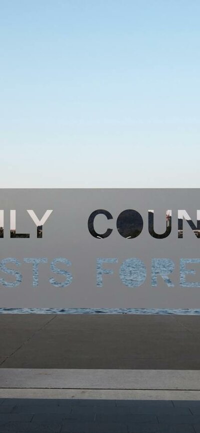 A metal sign that reads "Only Country Lasts Forever" positioned in front of Lake Burley Griffin.