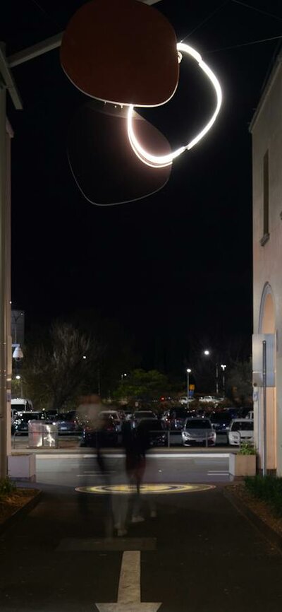 A neon sculpture hanging in an alley way at night.