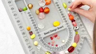 A grey bead design board on a table with hands reaching in moving beads around