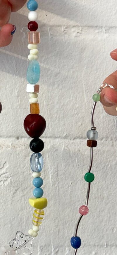 Two hands holding colourful beaded necklaces