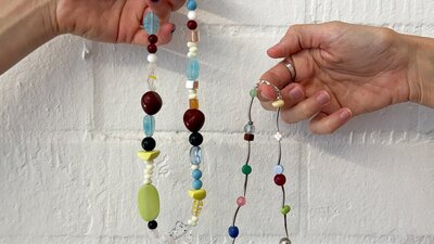Two hands holding colourful beaded necklaces