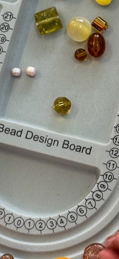 A grey bead design board on a table with hands reaching in moving beads around