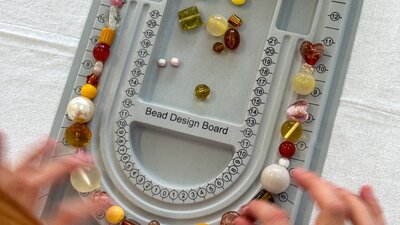 A grey bead design board on a table with hands reaching in moving beads around