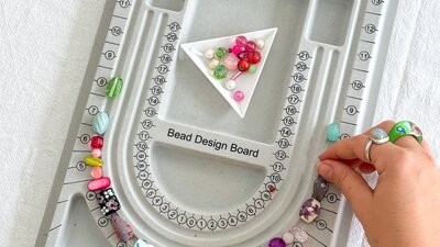 A grey bead design board on a table with hands reaching in moving beads around