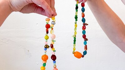 Two hands holding colourful beaded necklaces