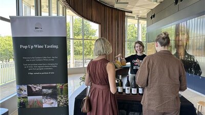 Pop-up cellar door at Canberra and Region Visitors Centre. Two people chatting to a vitner over bottles of wine.