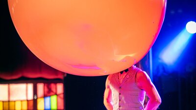 A muscular man wears a gigantic balloon on his head.