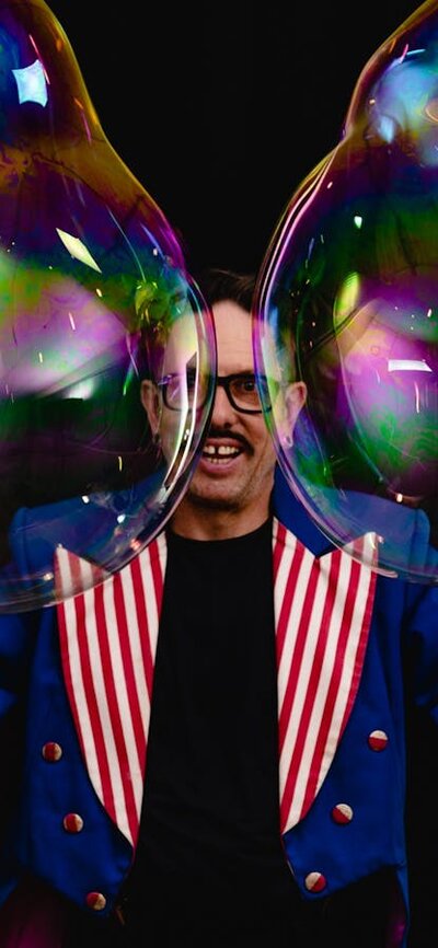 Dr Hubble's Bubbles Dr Hubble makes big bubbles while smiling at the Camera. He wears a fancy jacket in royal blue.