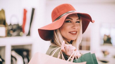 A woman wearing a wide-brimmed hat with a handbag over her shoulder smiling at the camera