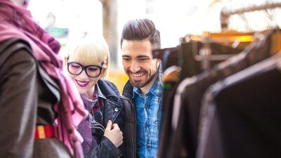 lady and a man smiling at clothing hanging up at an outdoor market