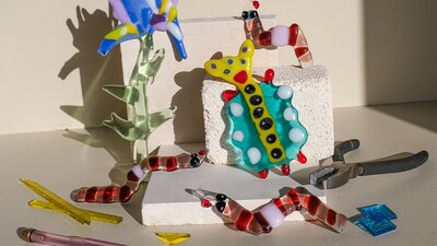 Colorful glass flowers, bugs and worms climbing over kiln blocks, surrounded by glass shards and too