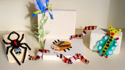 Colorful glass flowers, bugs and worms climbing over kiln blocks, surrounded by glass shards and too