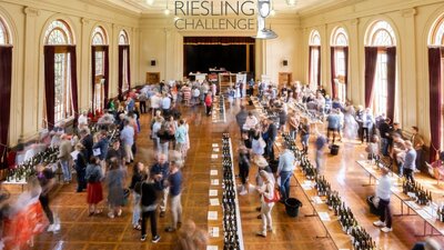 A community hall bustling with people milling around tables the people are tasting wines