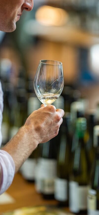 a man sips from a wine glass while looking at wine bottles