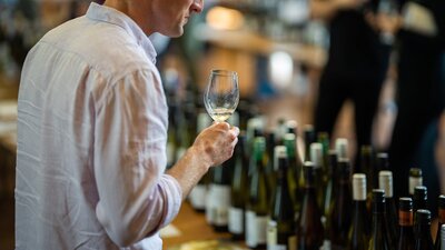 a man sips from a wine glass while looking at wine bottles